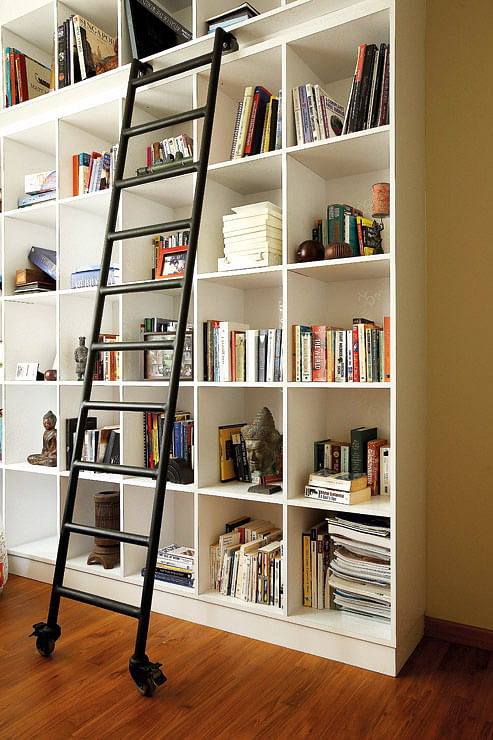 A spray-painted roller ladder allows access to the upper compartments of the built-in floor-to-ceiling shelves.
