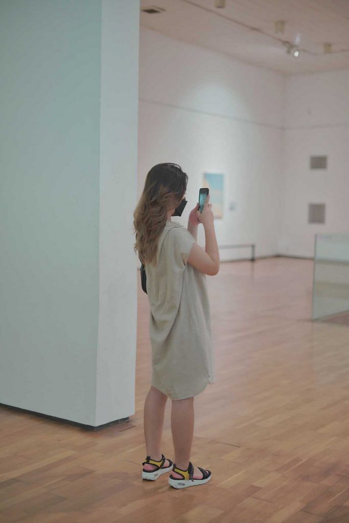 Woman at an art gallery taking a photograph of an art work with her mobile phone. Photo from Pexels Masa Multimedia.