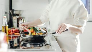 Woman cooking vegetables in a pan on an induction stove.